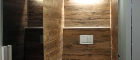 A modern bathroom with wooden panel walls, a toilet, a trash bin, and a small trash can.