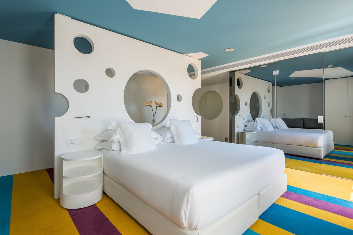 A modern bedroom with a large bed, a bedside table, and a mirror.