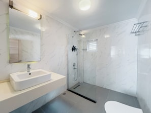 Un baño moderno con ducha de vidrio, lavamanos blanco y un espejo grande.