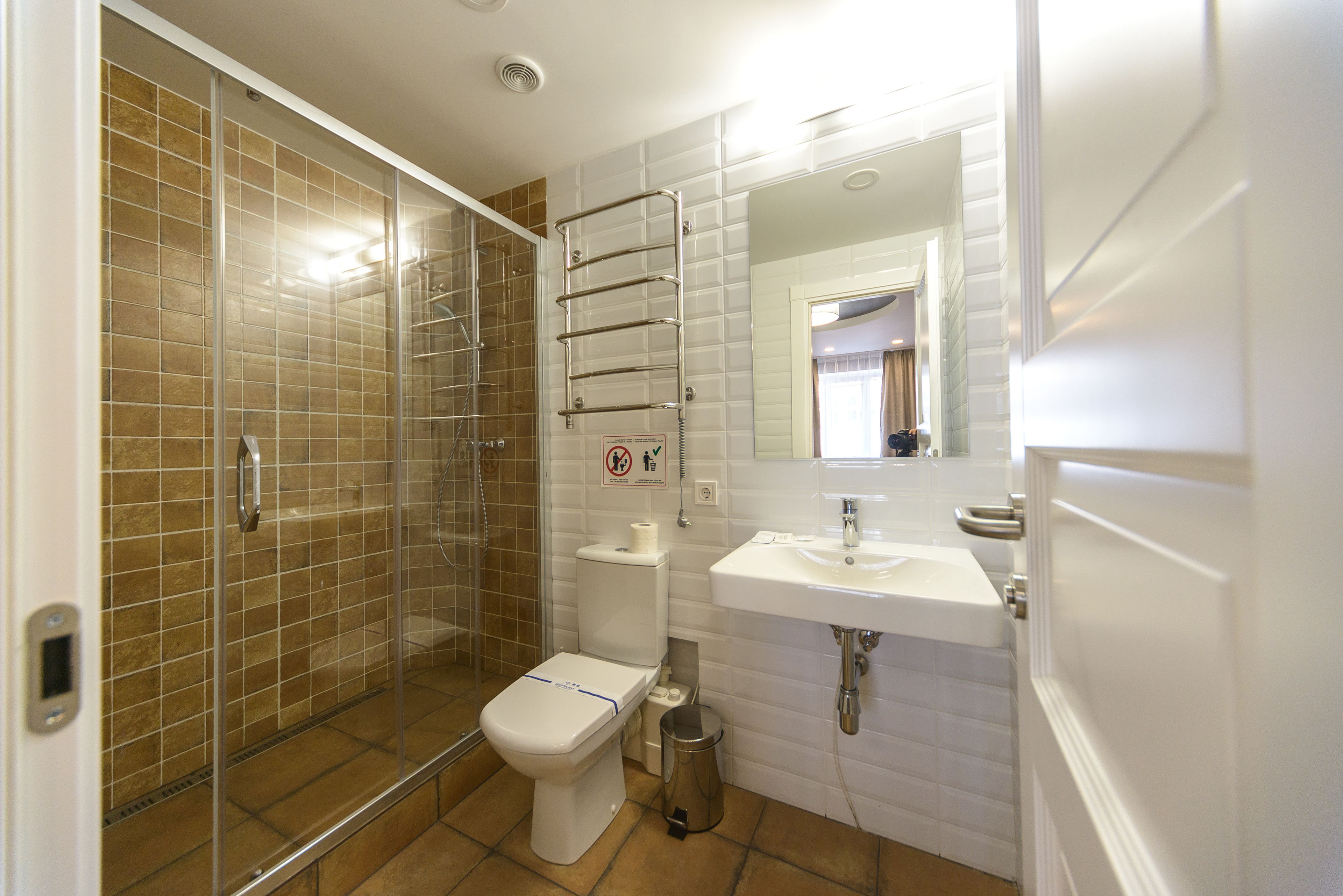 A bathroom with a glass-enclosed shower, a toilet, a sink, and a trash can.