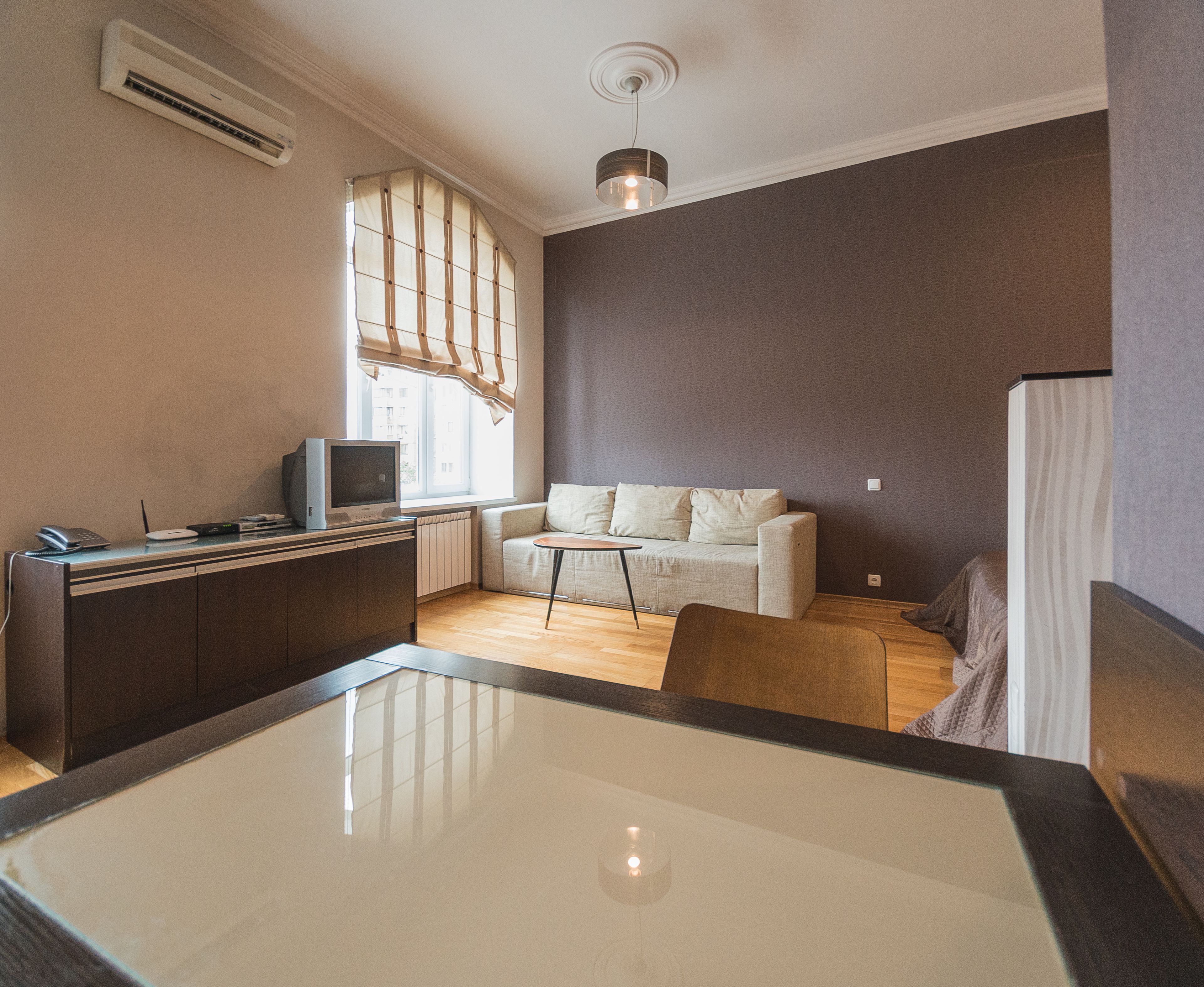 A modern living room with a sofa, a coffee table, a TV, and a dining area with a glass table.