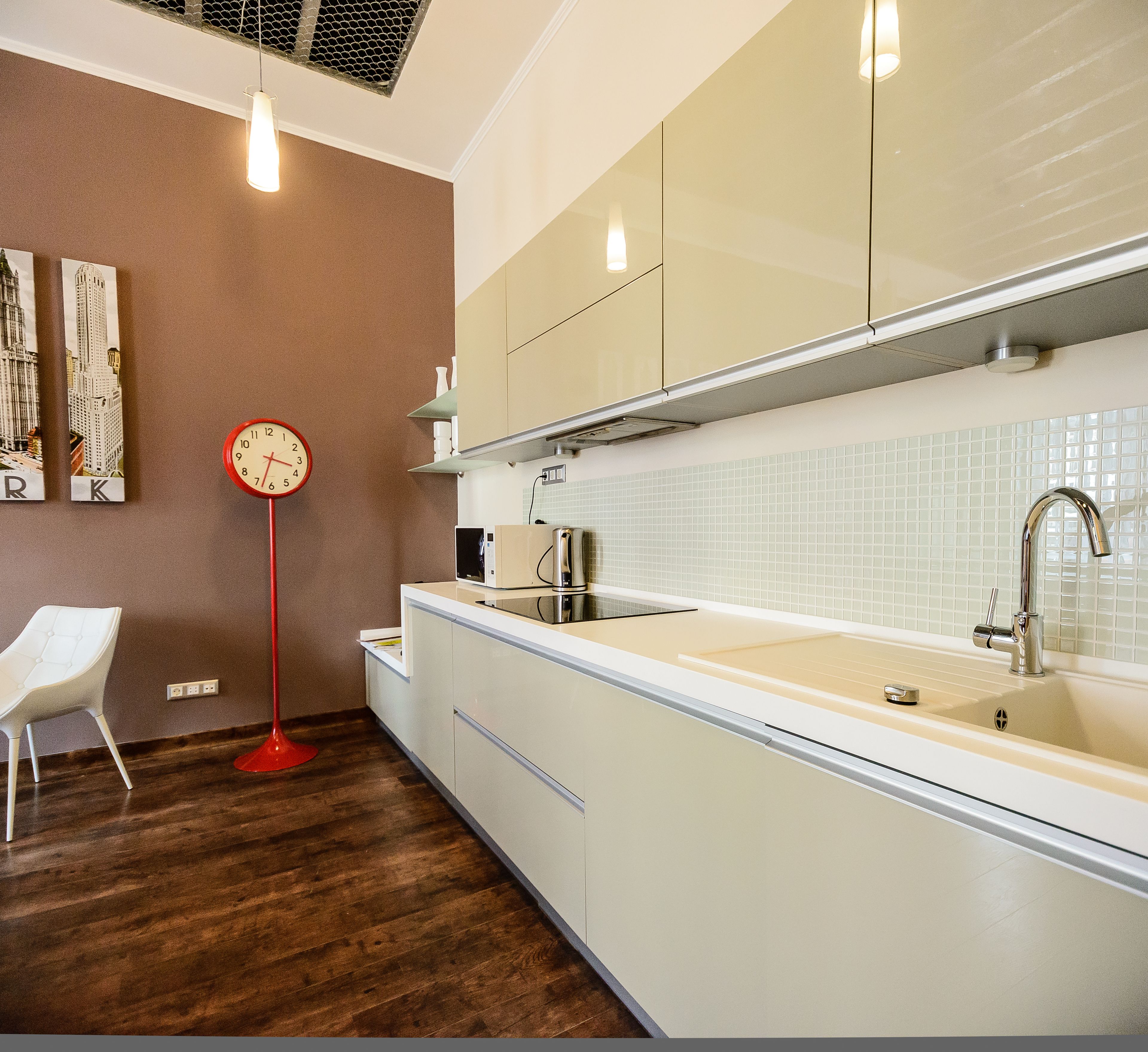 A modern kitchen with white cabinets, a stainless steel sink, and a red floor lamp.