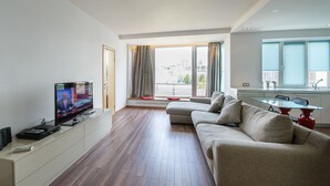 A modern living room with a flat-screen TV, a sofa, a glass coffee table, and a dining area with a red table and chairs. - Partner Guest House Saksahans'koho (Kyiv)