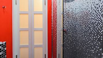 Ein Badezimmer mit roter Wand, weißer Tür und einer Duschkabine mit schwarz-weißen Mosaikfliesen.
