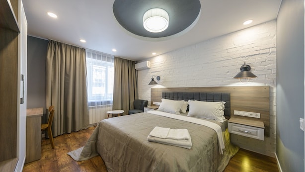 A modern bedroom with a large bed, a round ceiling light, a wooden headboard, and a small bedside table with a lamp. - Partner Guest House Saksahans'koho (Kyiv)