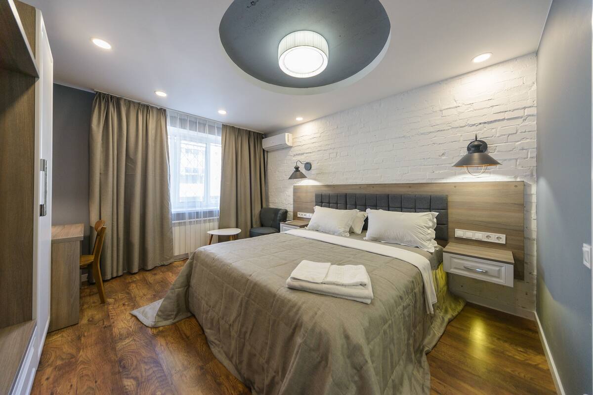 Un dormitorio moderno con una cama grande, una lámpara de techo redonda, un cabecero de madera y una mesita de noche pequeña con una lámpara.