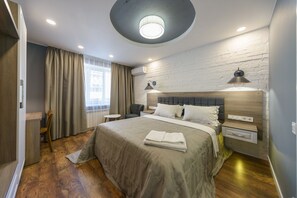A modern bedroom with a large bed, a round ceiling light, a wooden headboard, and a small bedside table with a lamp. - Partner Guest House Saksahans'koho (Kyiv)