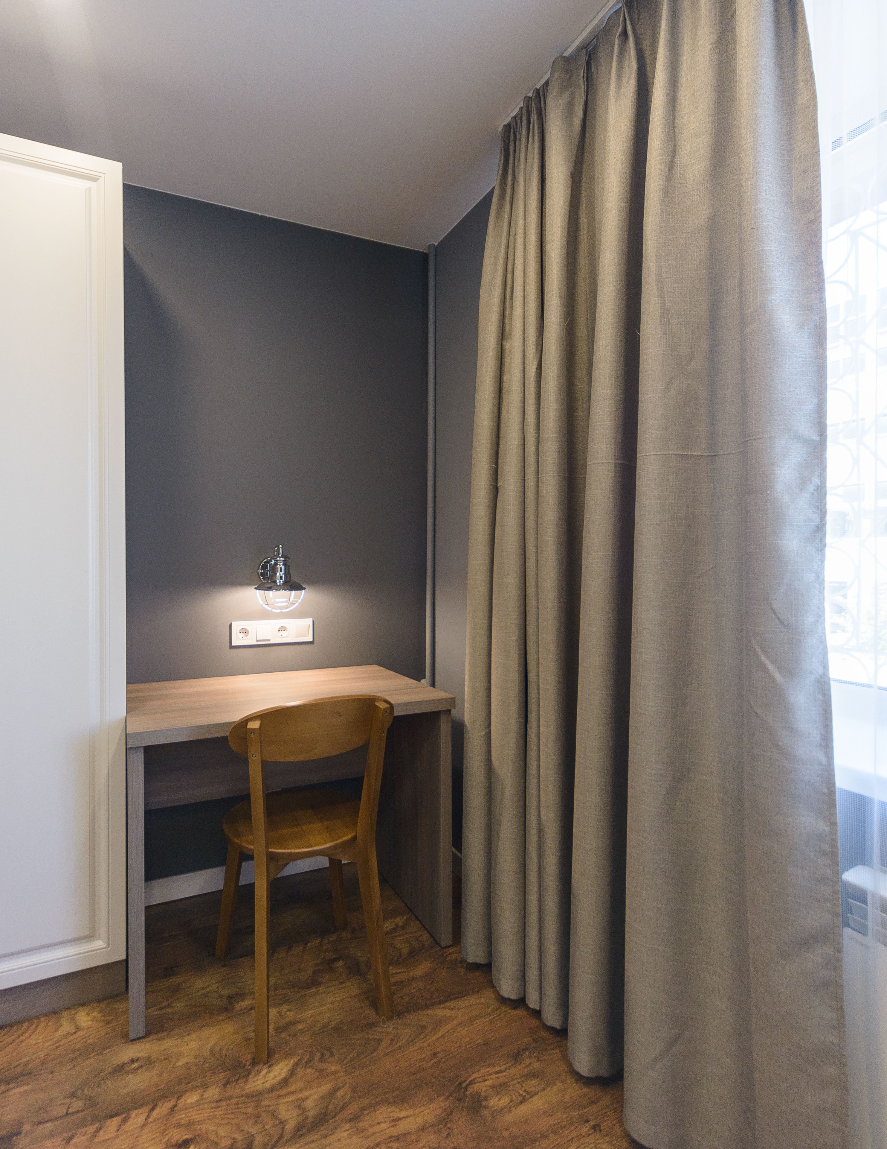 Une pièce de taille modeste, avec un bureau en bois, une chaise et une fenêtre avec des rideaux.