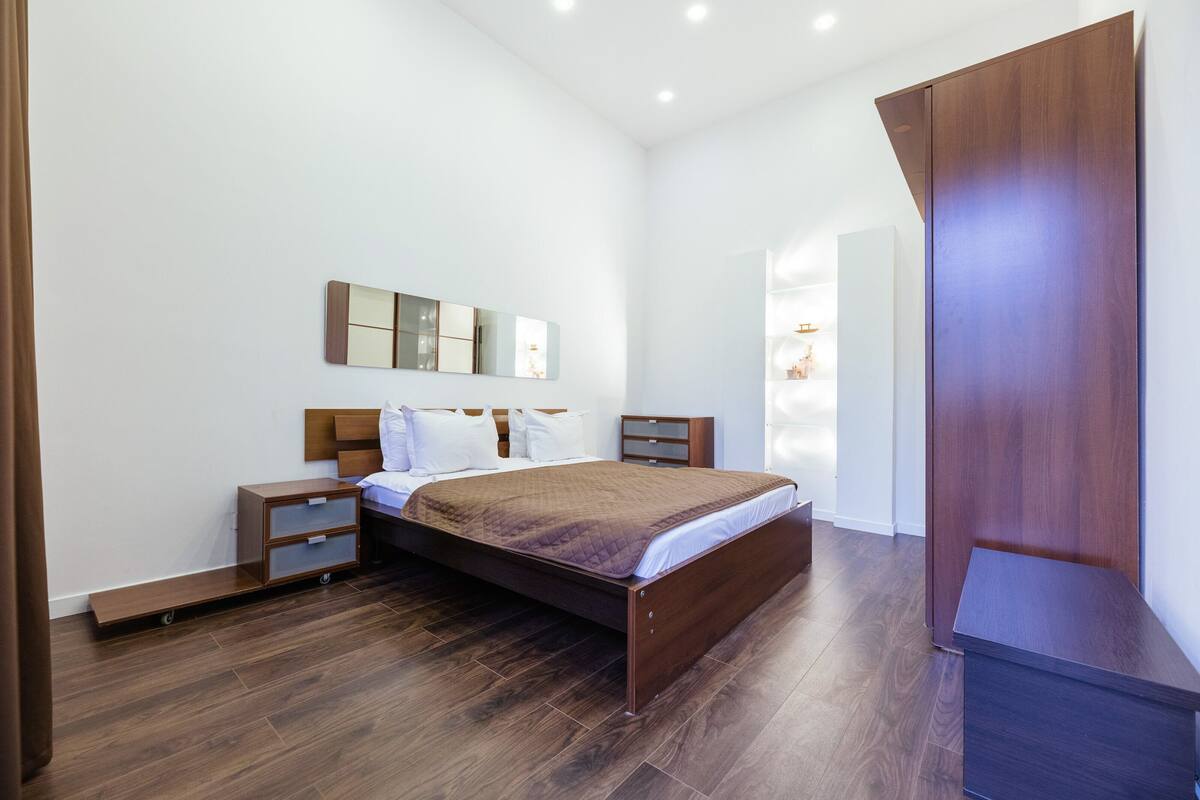 Un dormitorio moderno con una cama de madera, una mesita de noche, un aparador y un espejo grande en la pared.
