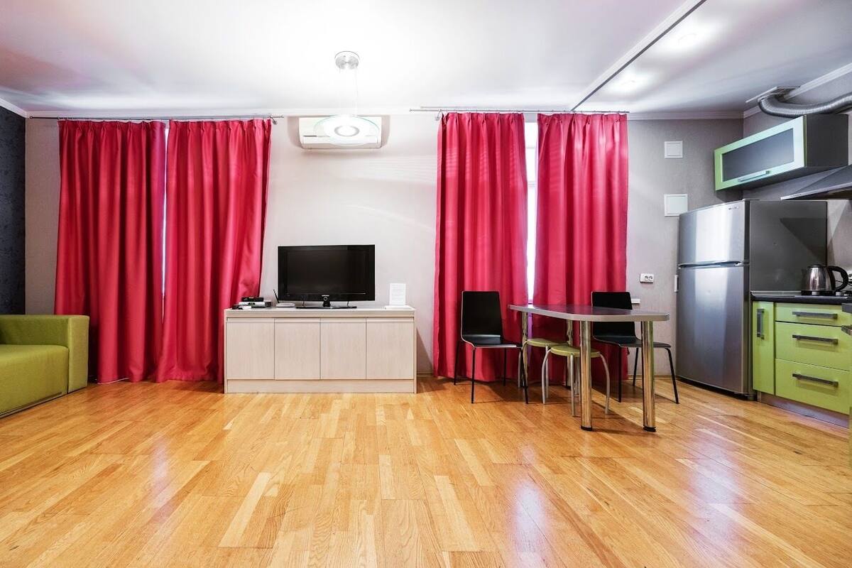 Un espacio habitable compacto con sofá, televisión sobre un mueble, mesa de comedor con sillas y una zona de cocina con refrigerador y microondas.