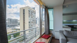 A modern apartment with a large window, a grey sofa, and a red cushion on a wooden bench. - Partner Guest House Saksahans'koho (Kyiv)