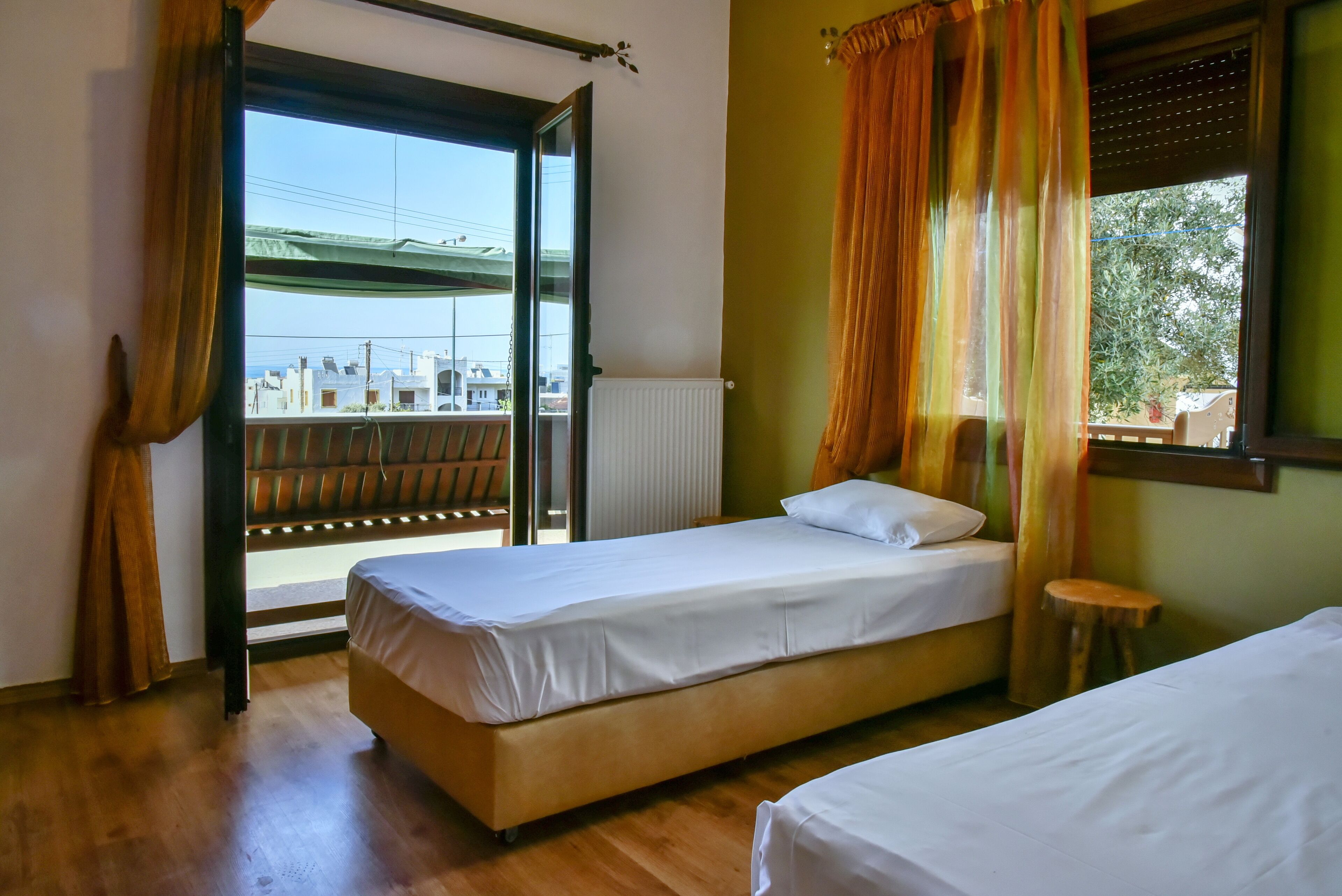 Une chambre à coucher avec un lit, une fenêtre avec des rideaux, un radiateur et une vue sur les bâtiments à l’extérieur.