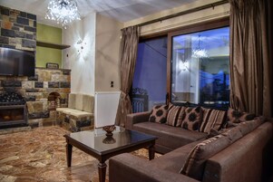Una sala de estar con chimenea de piedra, un sofá con cojines estampados, una mesa de centro de vidrio y vistas a la ciudad a través de un ventanal grande.