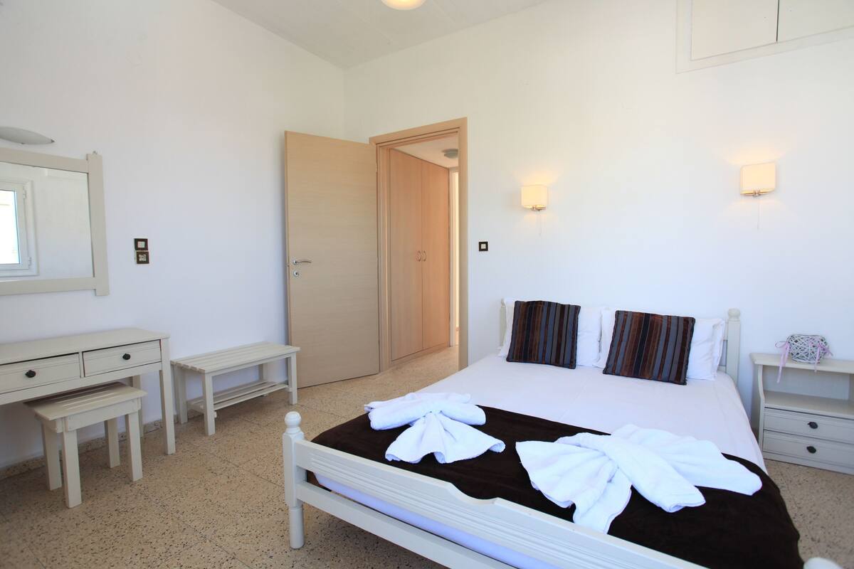 A neatly arranged bedroom with a bed, bedside tables, a desk, and a wardrobe.