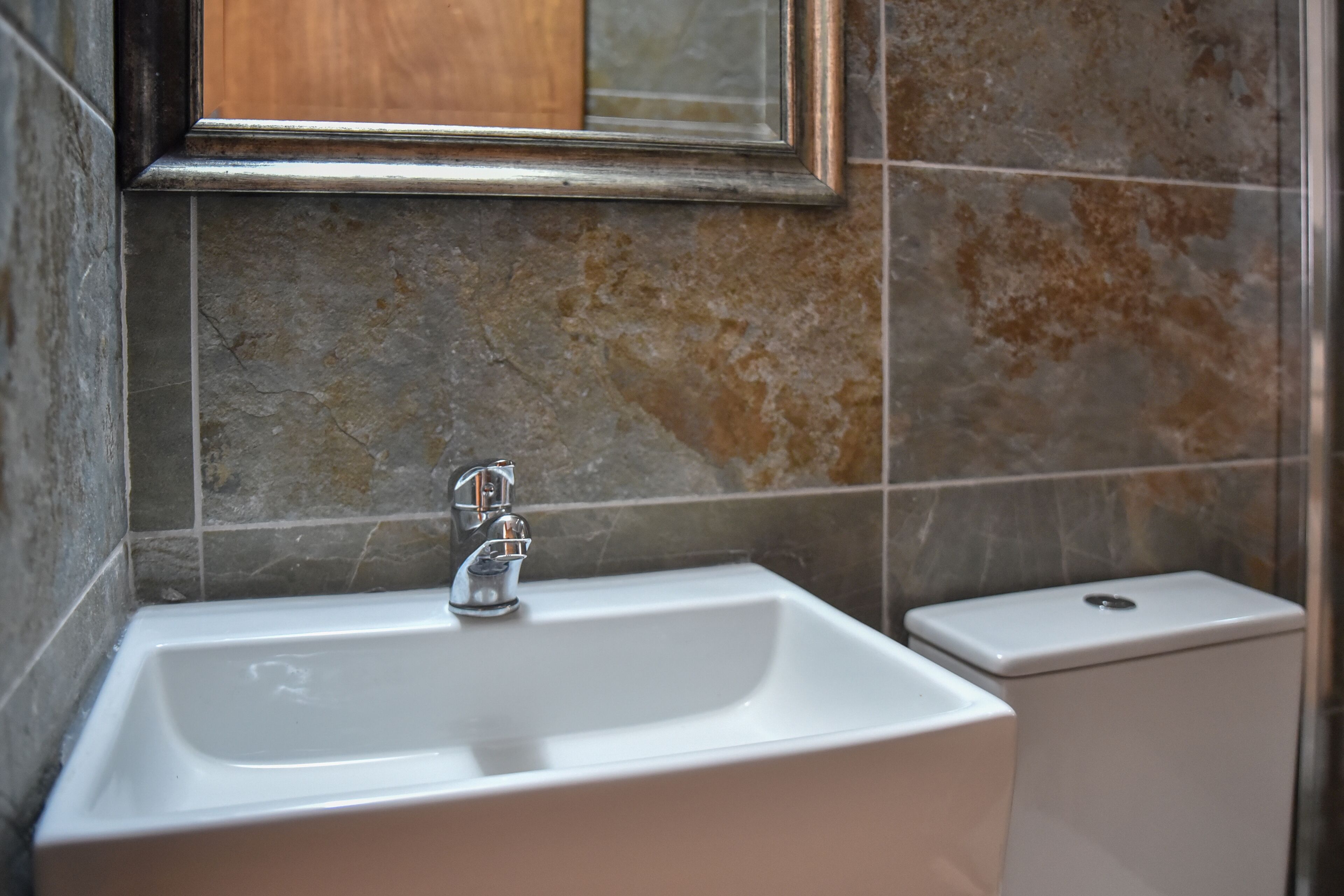 Un baño con un lavamanos rectangular, un espejo encima y un inodoro a la derecha.