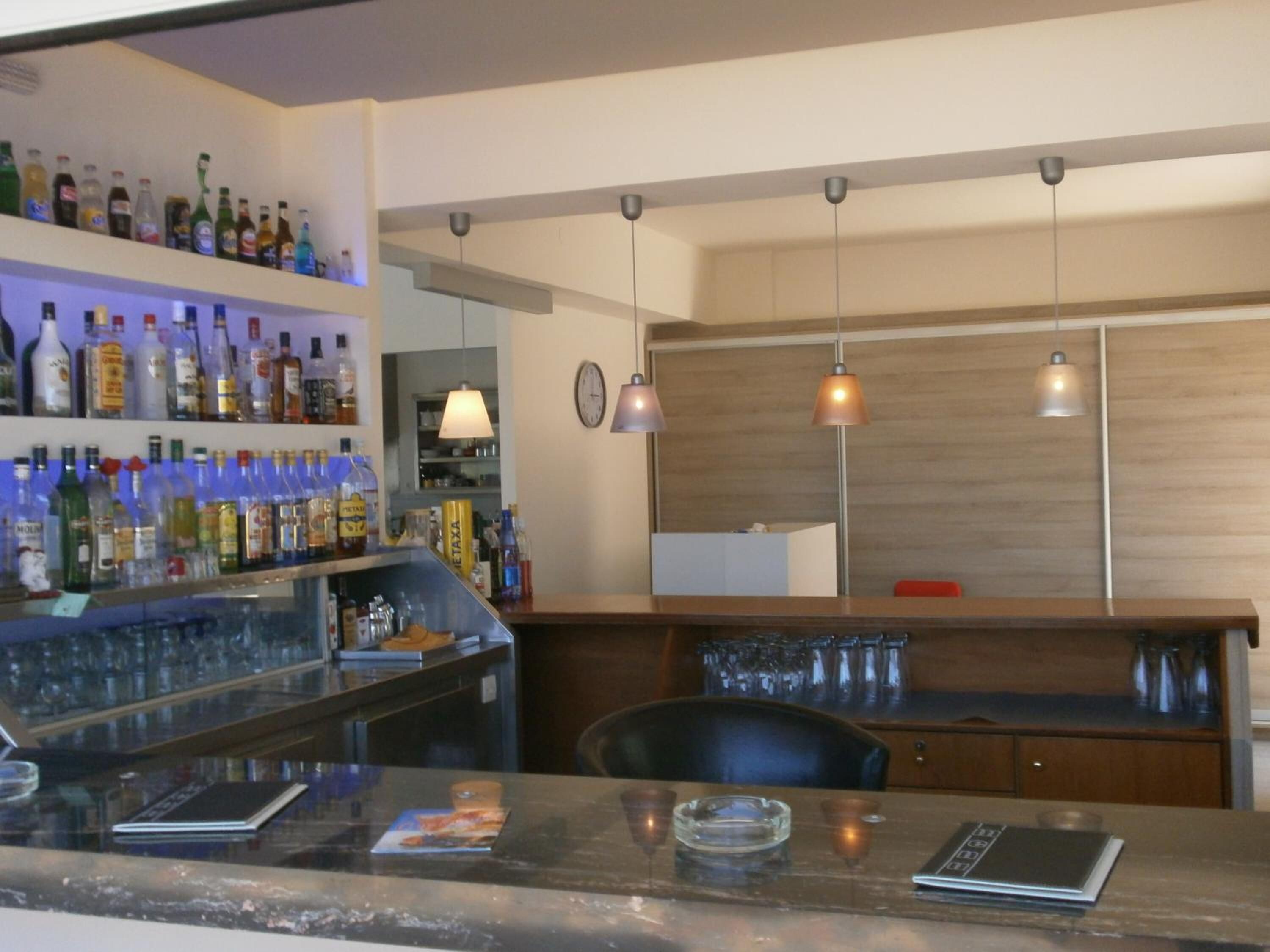 Zona de bar con estantes llenos de botellas de licores, una barra con carta y luminarias colgantes.