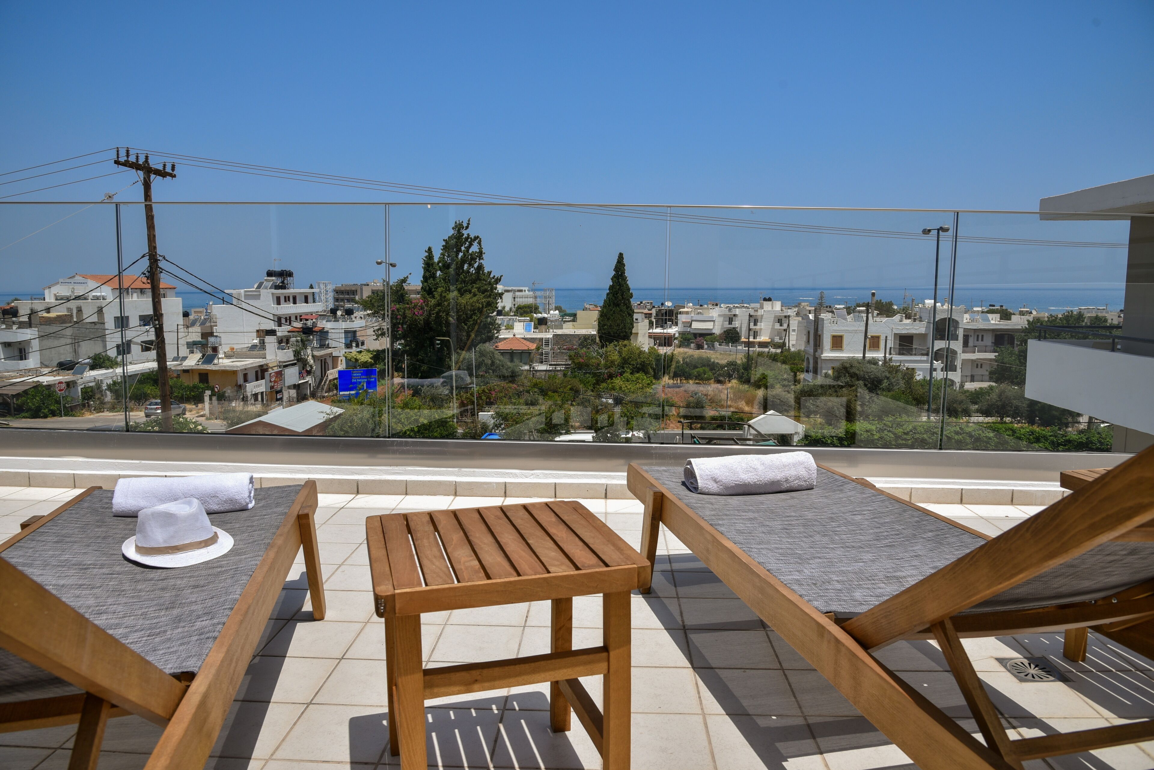 A balcony with wooden furniture, a view of the sea, and buildings in the background.