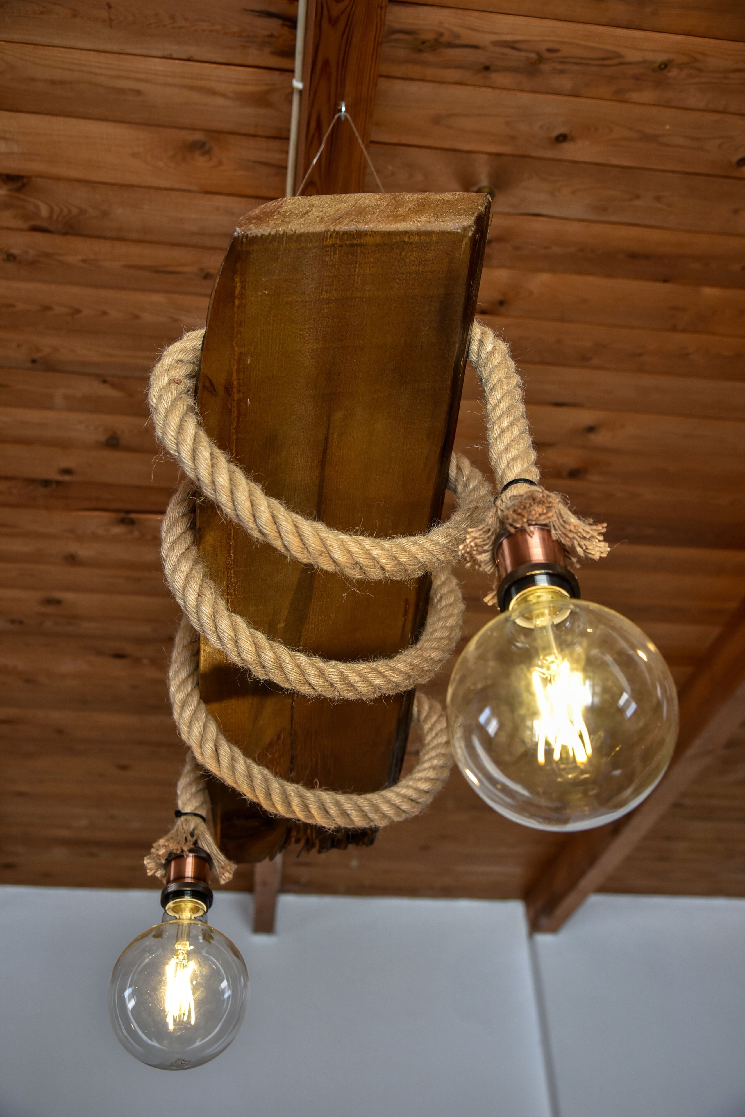 Un plafond en bois, avec une corde et deux lampes à ampoules en verre.
