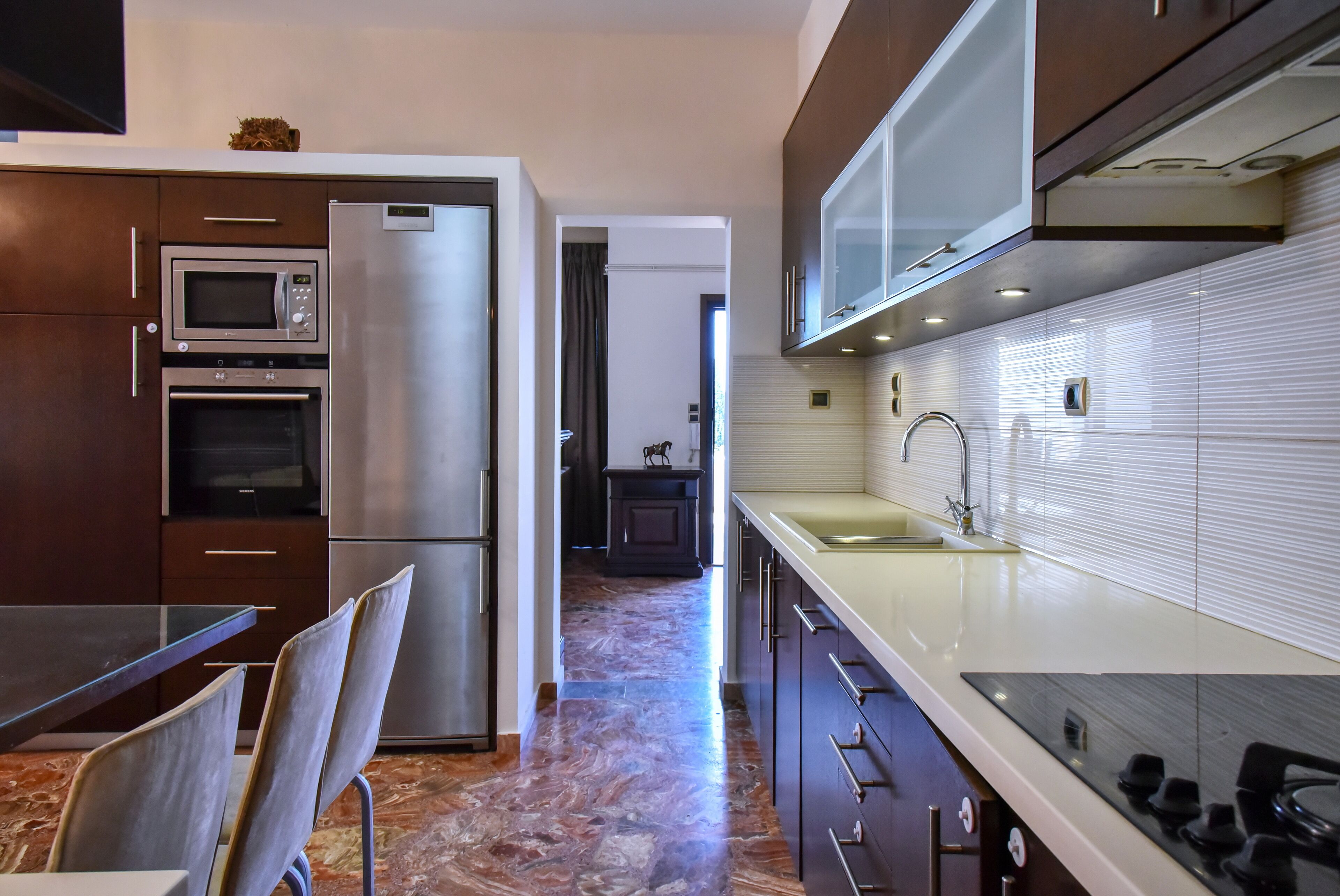 A modern kitchen with a refrigerator, microwave, oven, and a dining area with chairs and a table.