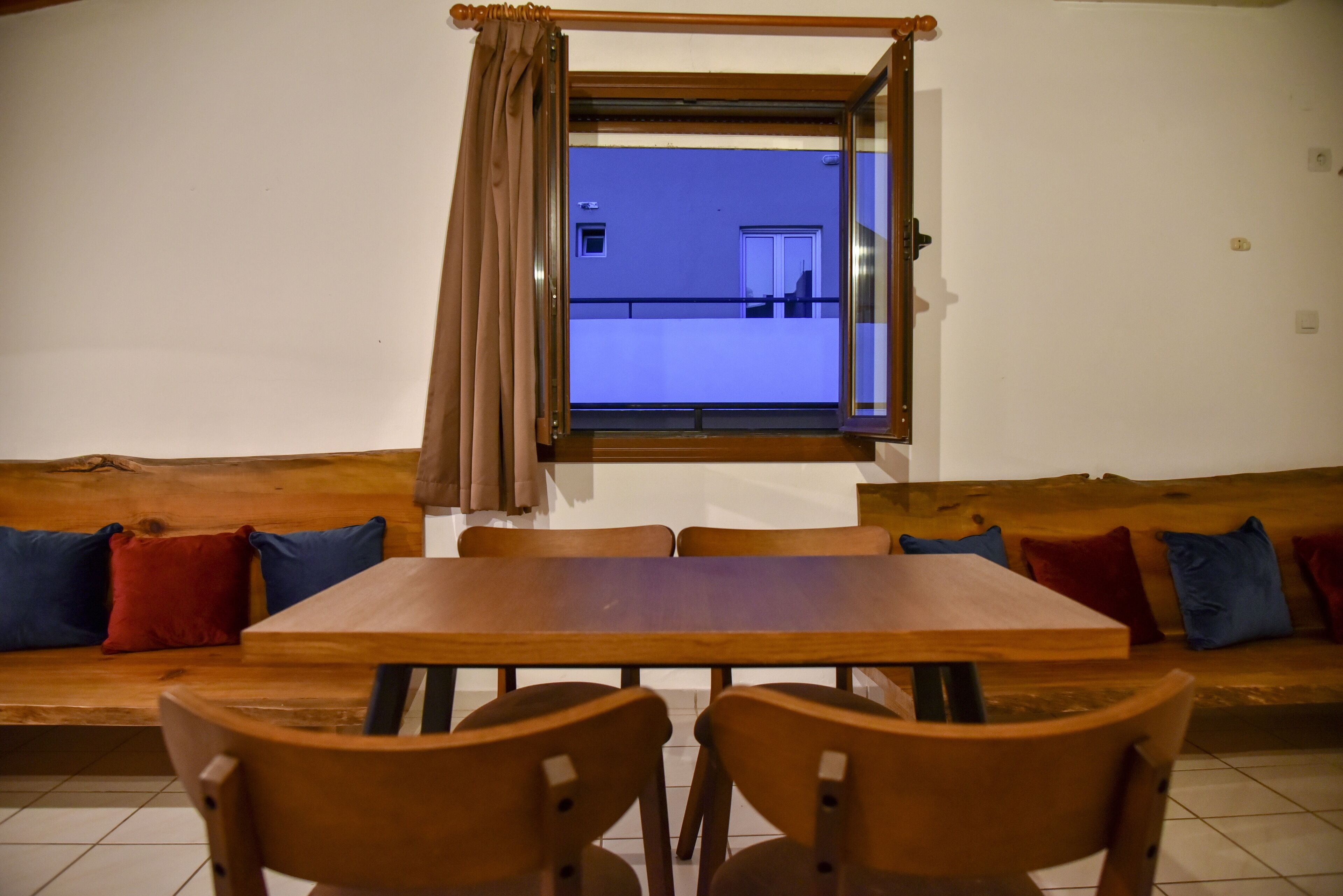 Una zona pranzo con un tavolo e sedie in legno, una panca con cuscini e una finestra con tende.