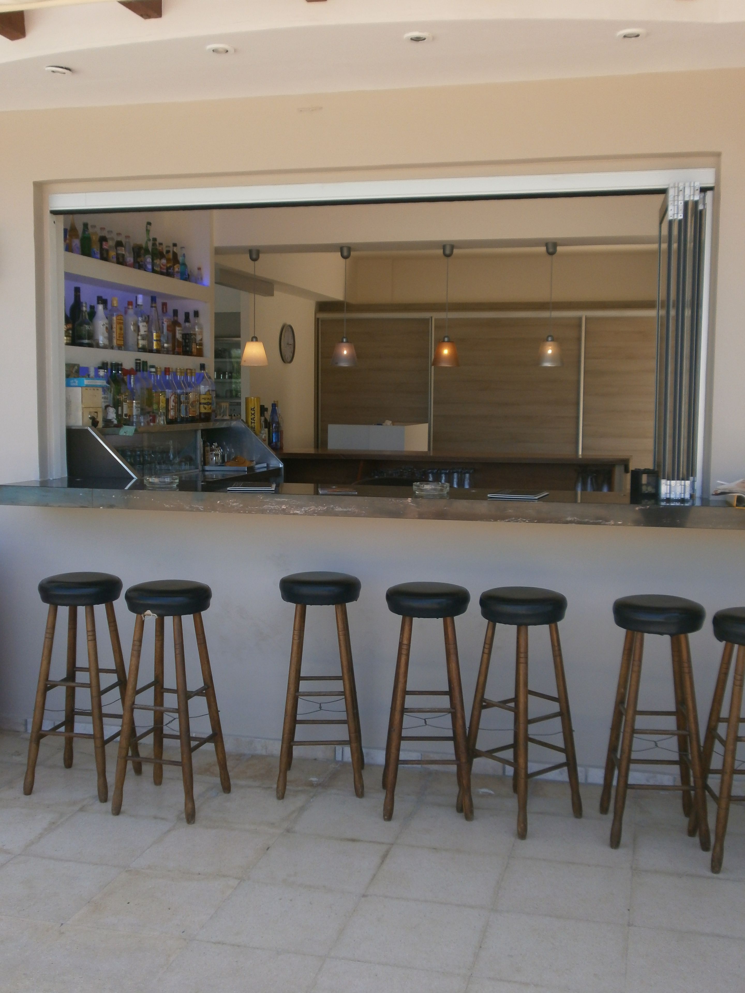 Una zona de bar con taburetes y una estantería llena de botellas.
