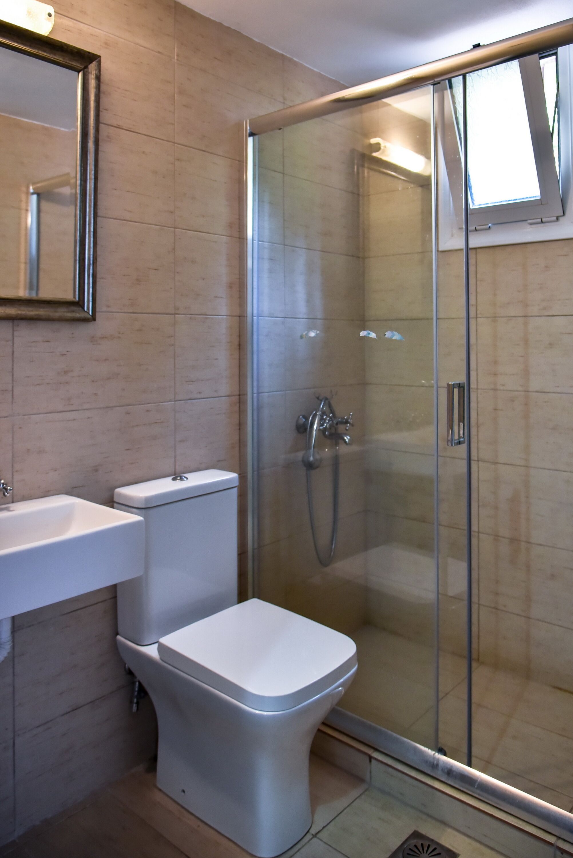 Een badkamer met toilet, wastafel en een douchecabine met glazen wanden.