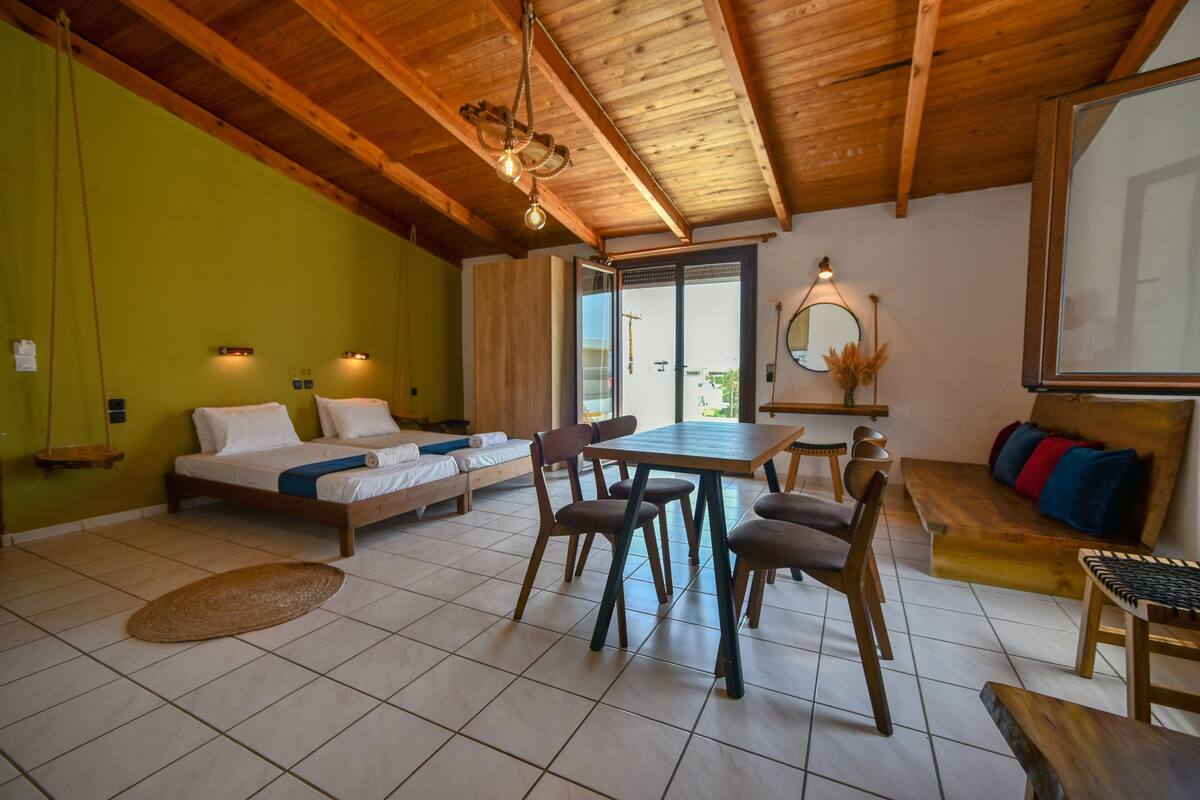 A room with a bed, a dining table with chairs, a bench, a mirror, and a view of the outdoors.