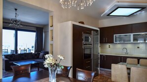 Cozinha moderna com armários escuros, forno embutido e micro-ondas. Há uma área de refeições com mesa e cadeiras de madeira, e um lustre acima.
