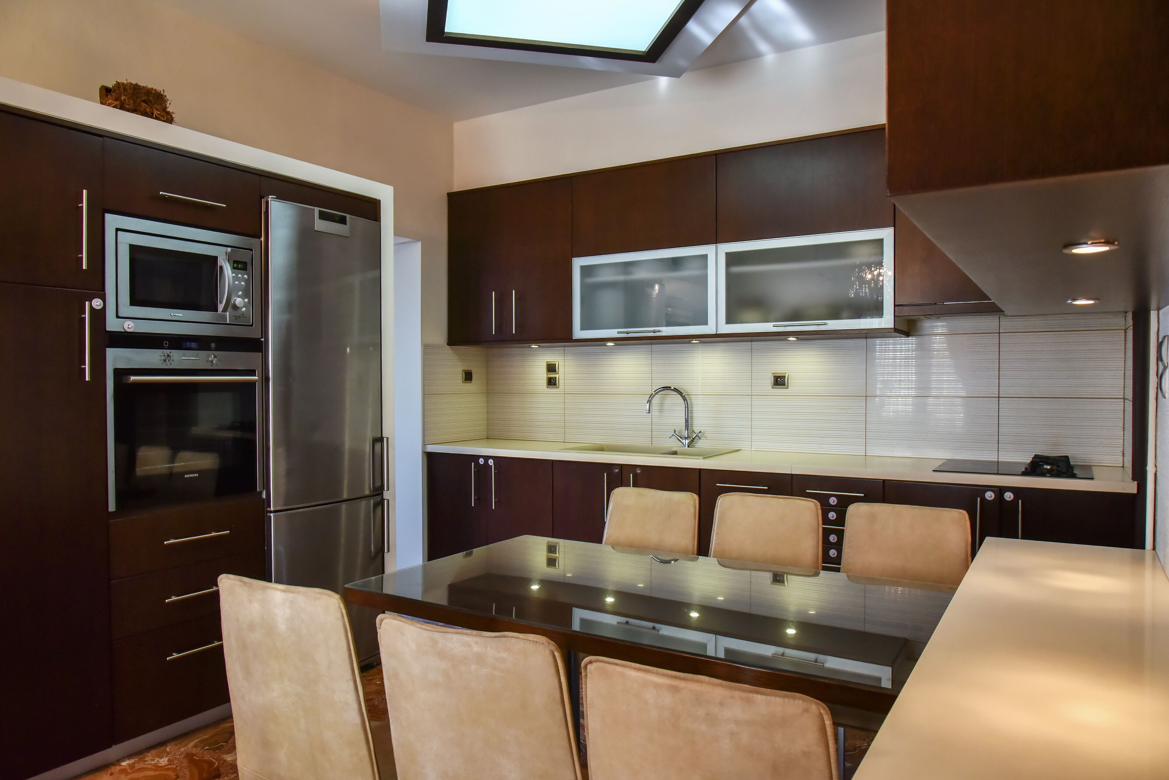 A modern kitchen with built-in appliances, a dining area with chairs, and a skylight above.