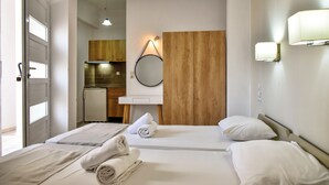 Quarto de hotel com duas camas, parede de painel de madeira, pequeno espaço de cozinha e banheiro visível através de uma porta aberta.