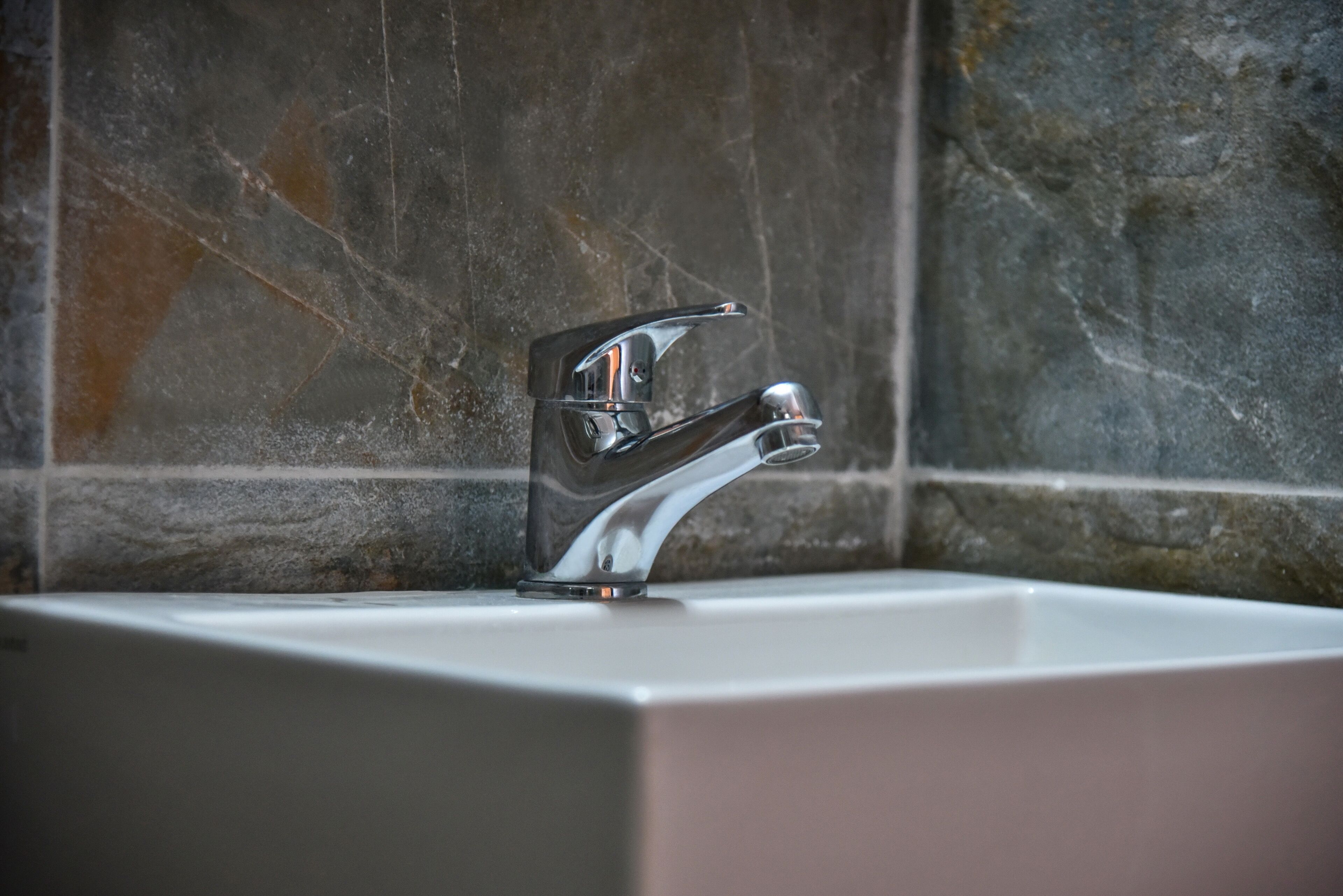 A bathroom with a modern chrome faucet and a rectangular sink against a tiled wall.