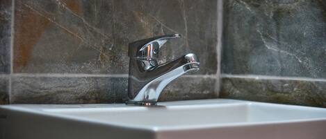 A bathroom with a modern chrome faucet and a rectangular sink against a tiled wall.