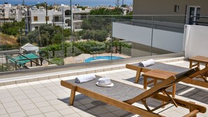 Terraço no telhado com espreguiçadeiras, piscina e vista para o mar e prédios.