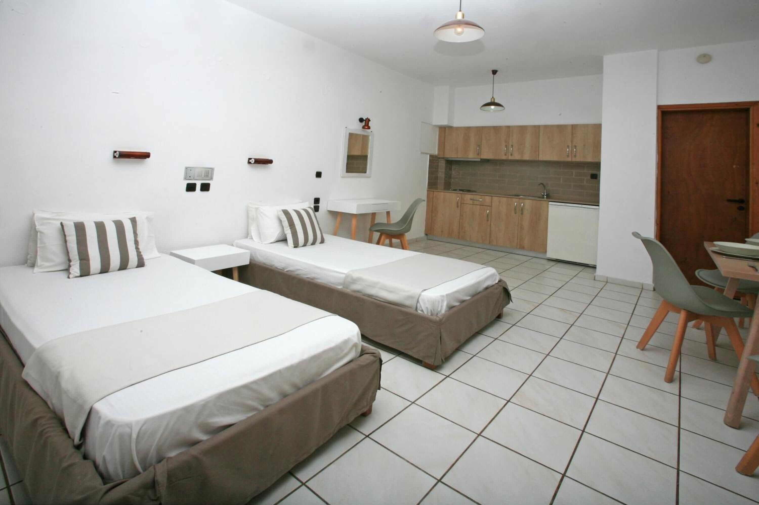 A compact hotel room with two single beds, a small kitchenette, a dining area, and a bathroom.