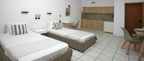 A compact hotel room with two single beds, a small kitchenette, a dining area, and a bathroom.