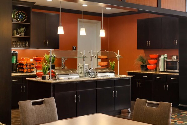 A modern kitchen with dark cabinetry, a central island, and pendant lighting. - Homewood Suites by Hilton Joplin (Joplin)