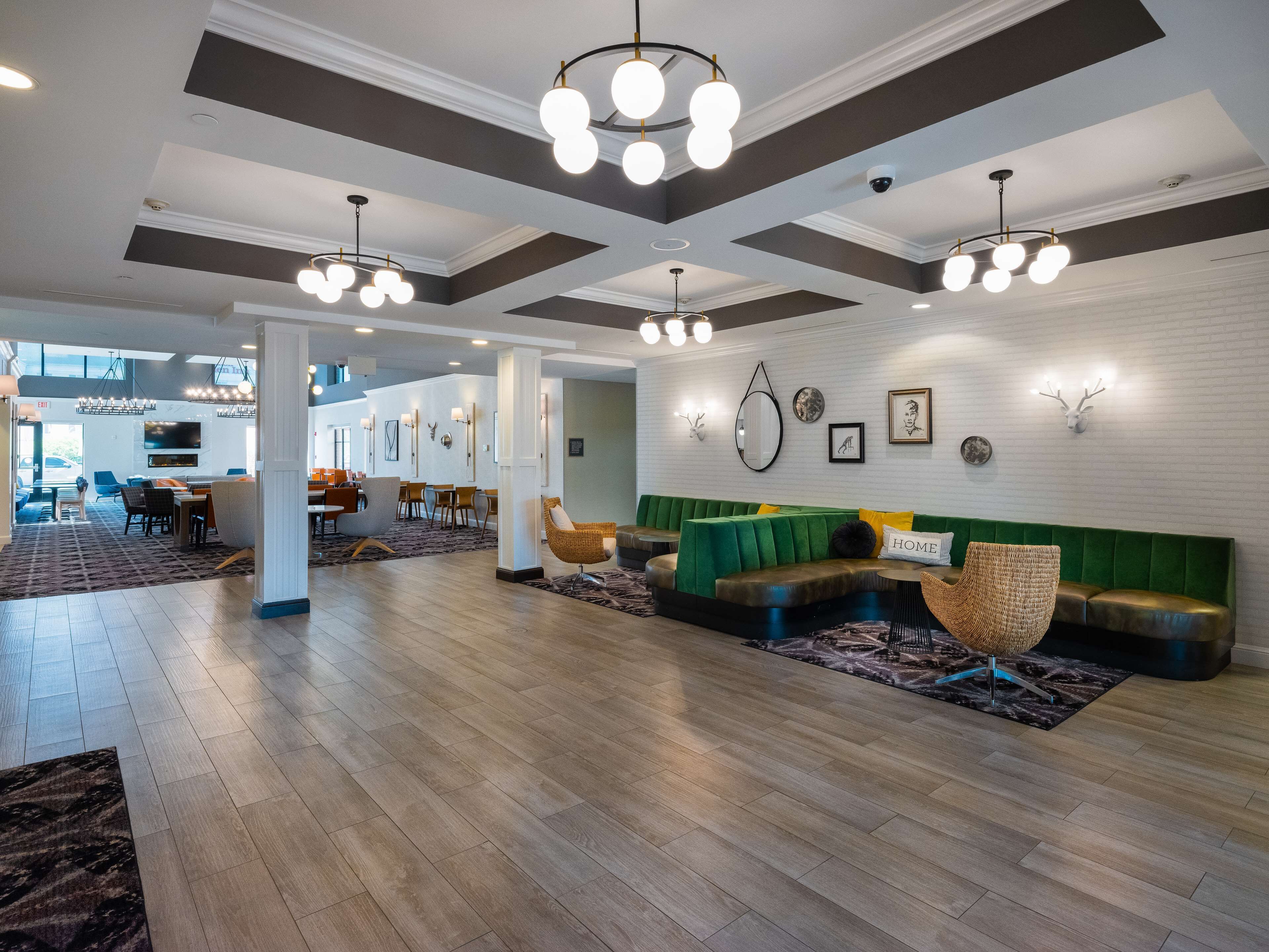 A spacious lobby with a green upholstered sofa, multiple seating areas, and a large window providing natural light.