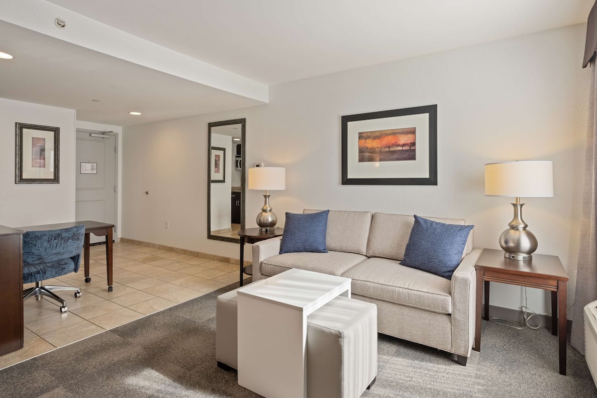 A modern hotel room with a sofa, a small table, a lamp, and a mirror.