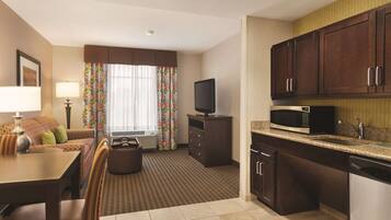 A hotel room with a dining area, kitchenette, and a television.