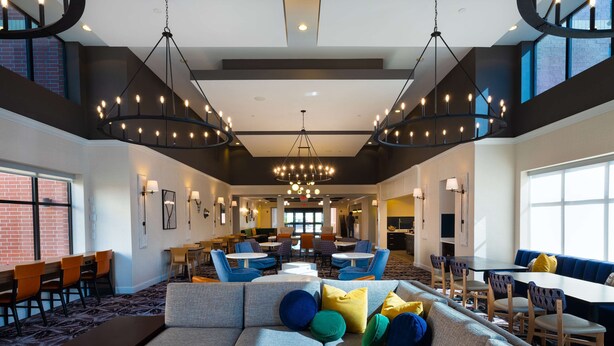 Un hall d’hôtel spacieux avec un espace salon central, de nombreuses tables et un grand lustre.