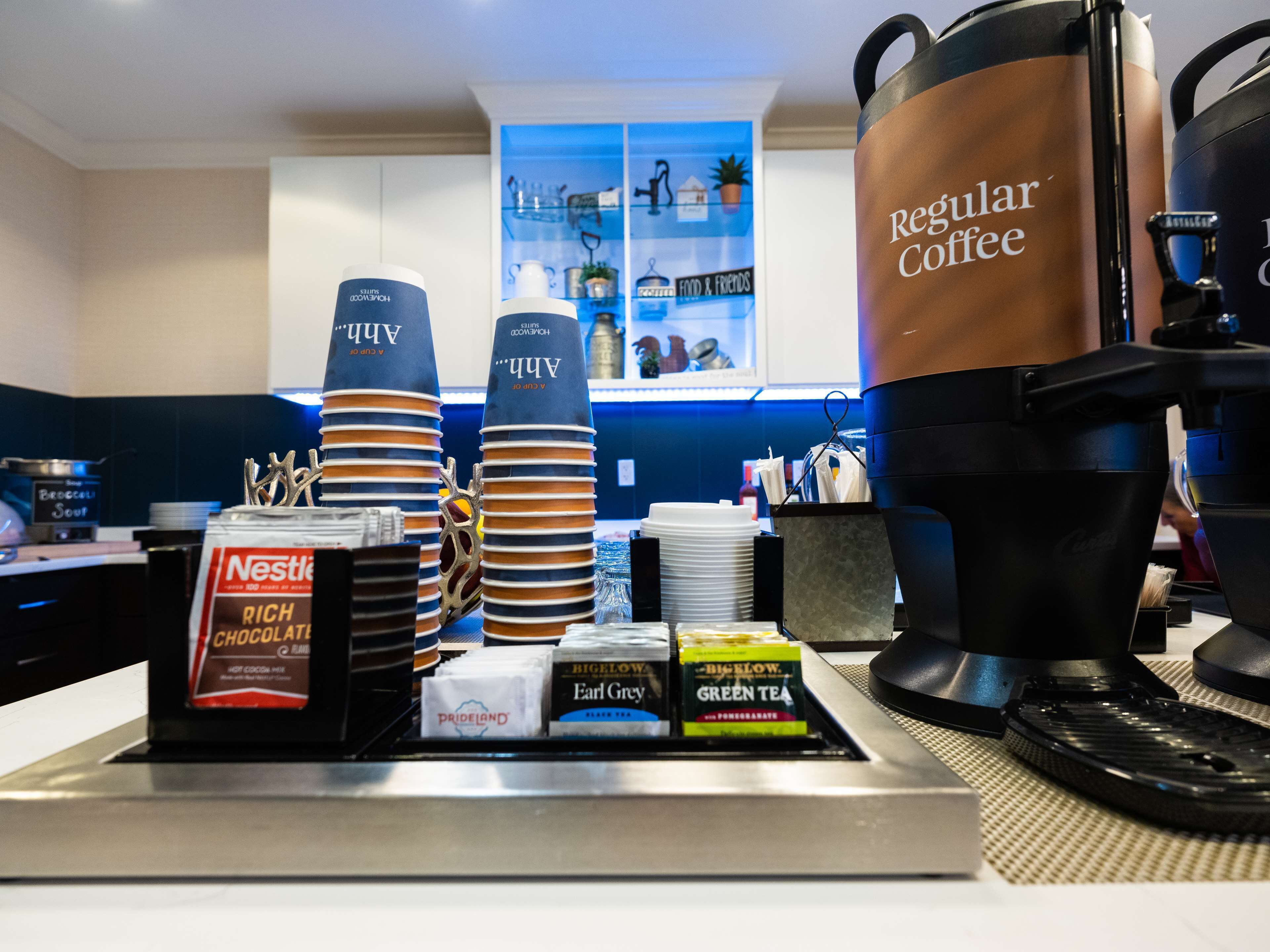 Una estación de café con una máquina de café, tazas y diferentes tipos de cápsulas.