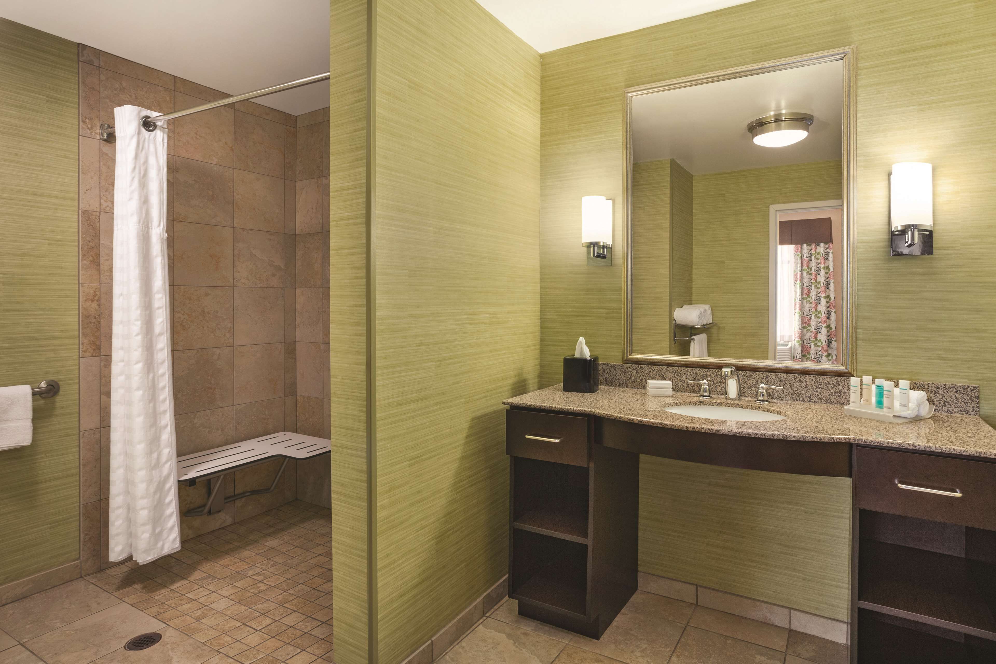 A bathroom with a shower, a sink with a mirror, and a bench.