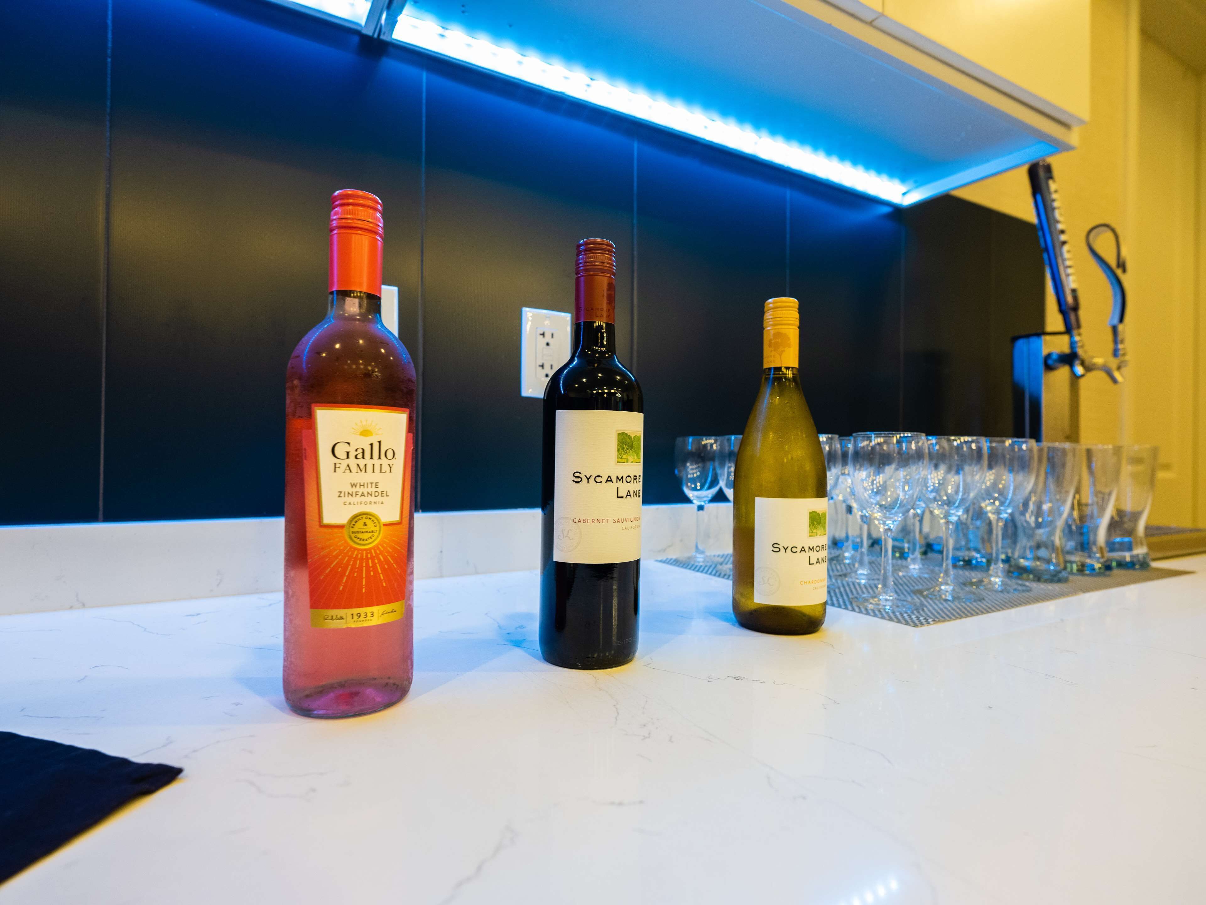 Three wine bottles on a counter with glasses behind them.
