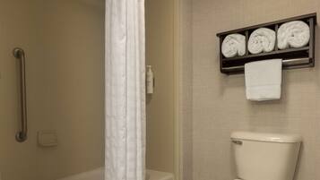 A bathroom with a bathtub, toilet, and a shelf with rolled towels.