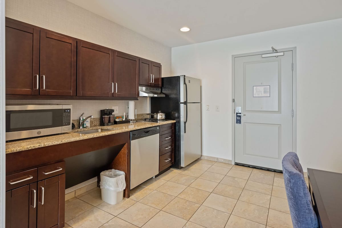 A compact kitchen with dark wooden cabinets, a stainless steel microwave, a black refrigerator, and a dishwasher.