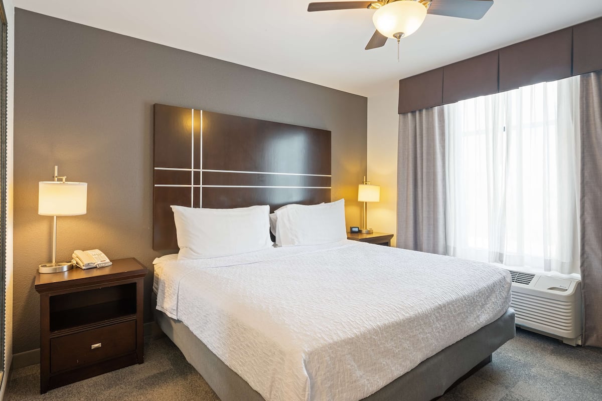 A hotel room with a large bed, two bedside tables, a ceiling fan, and a window with curtains.