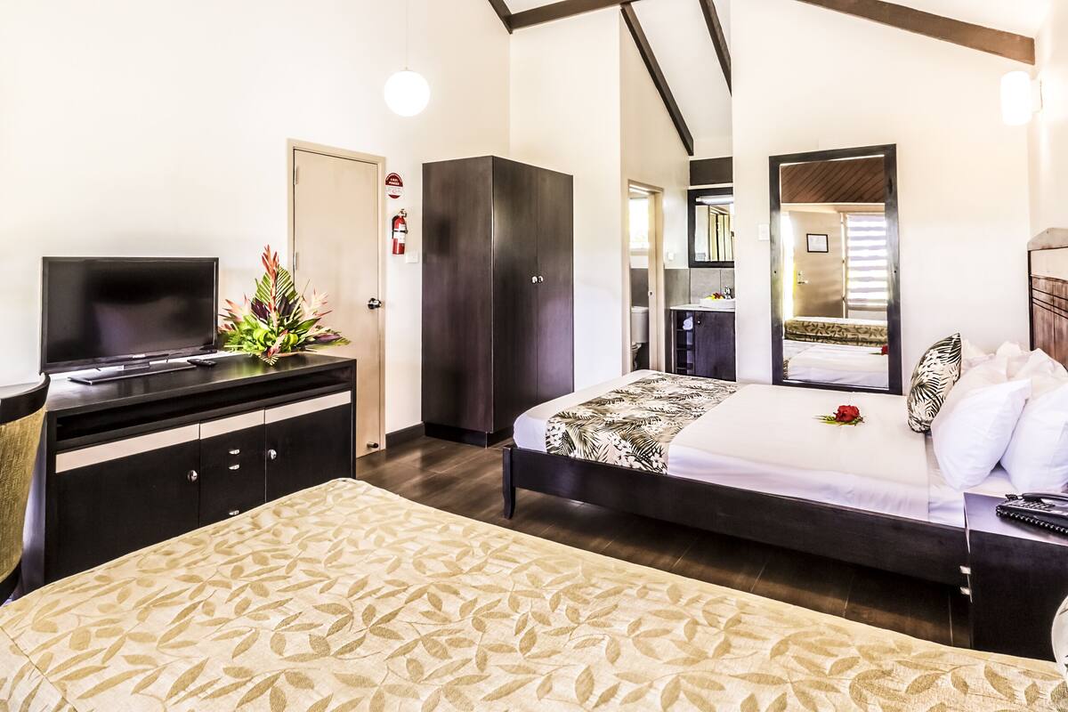 A hotel room with a bed, a desk with a TV, a wardrobe, and a bathroom visible through an open door.