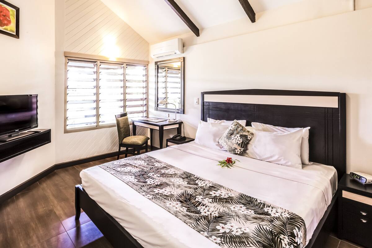 A hotel room with a bed, a desk, a TV, and a window with blinds.