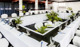 Un salón de conferencias con una larga mesa, sillas blancas y plantas en macetas.