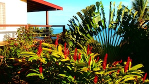 Un jardin tropical avec une grande variété de plantes et un bâtiment doté d’un toit rouge.